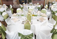 Table setup for a wedding with cloth napkins, silverware, chair covers, and centerpieces