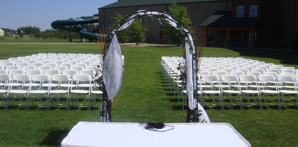 Outdoor wedding ceremony setup with an arch for the couple to stand under and white chairs for the guests